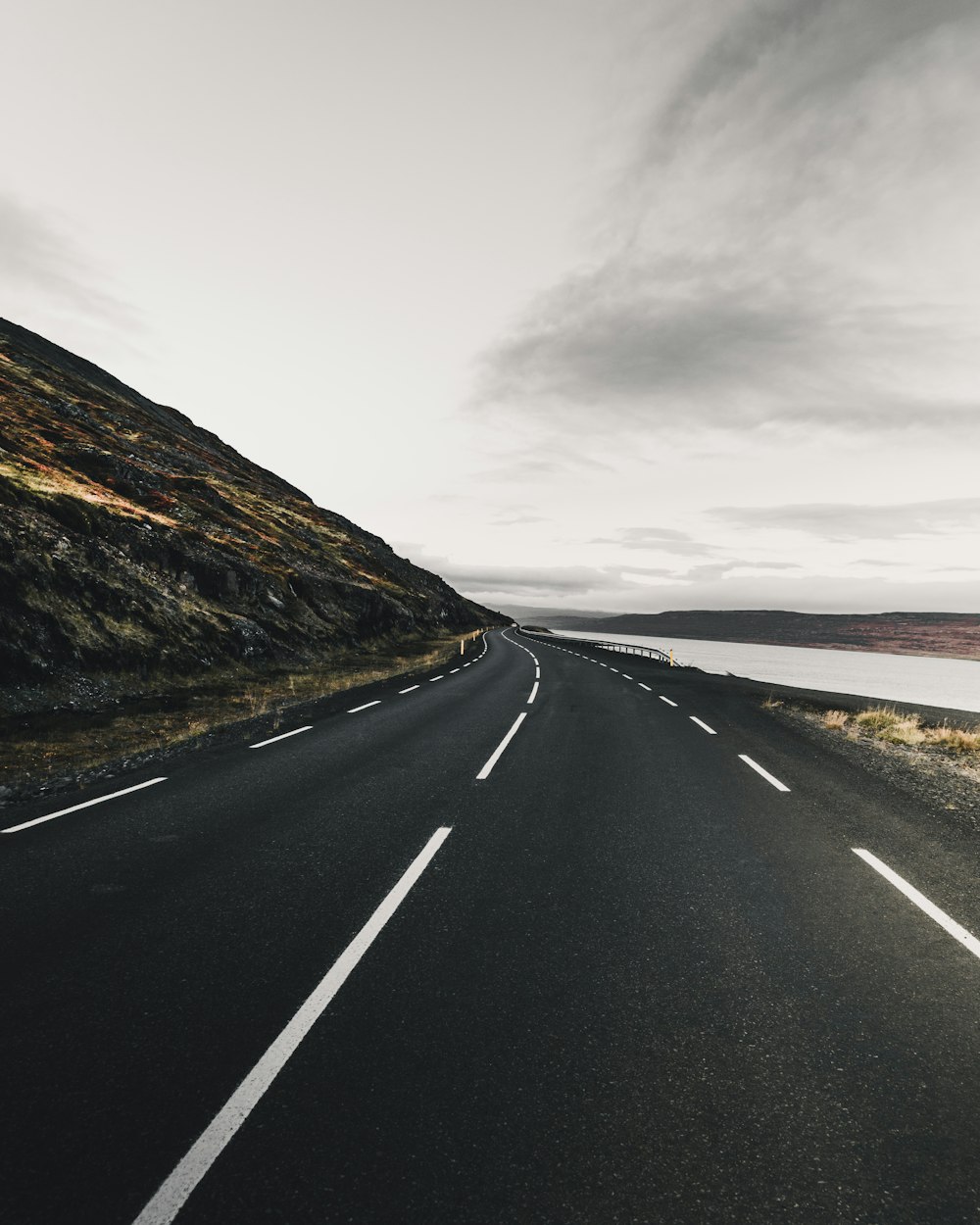 empty road between mountain and body of water