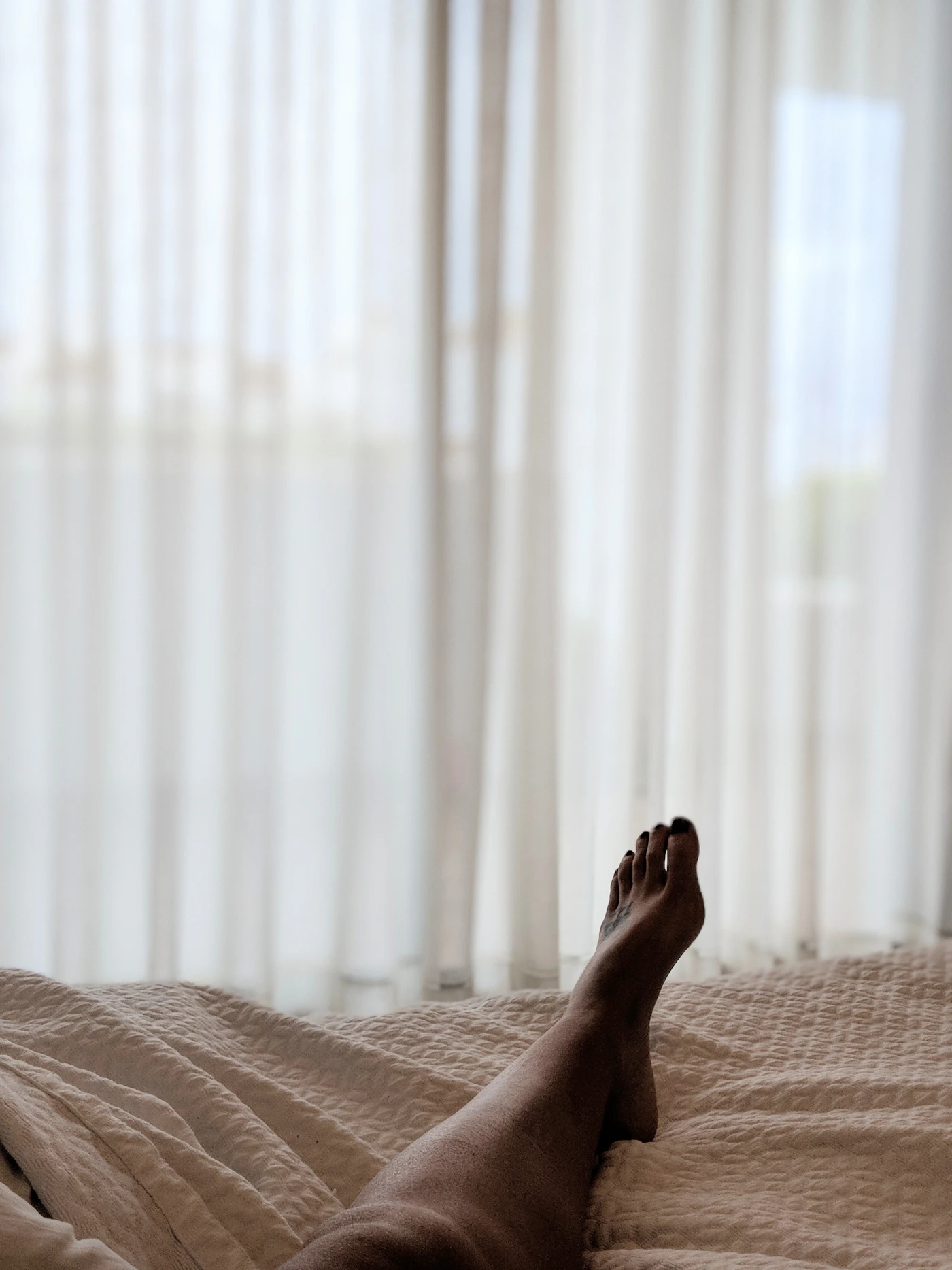 Cool-down: bare legs stretched out on a bed by sheer curtains