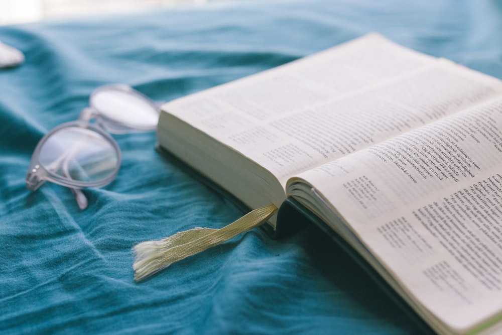 opened Bible near clear eyeglass on teal textile