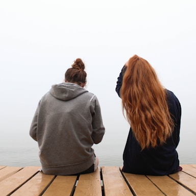 two women sitting on wooden dock over body of water
