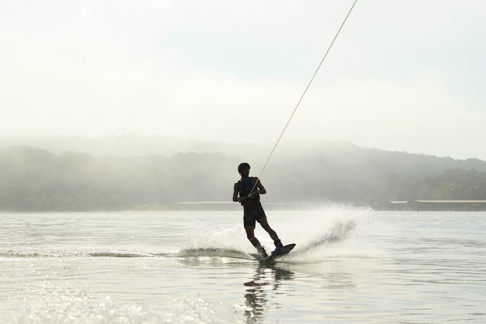 photo of man surfing on body of water and holding rope