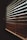 A close-up view of wooden blinds partially closed, casting shadows and allowing diffused light to pass through. The slats are positioned diagonally, creating an interplay of light and shadow on their surface.