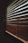 A close-up view of wooden blinds partially closed, casting shadows and allowing diffused light to pass through. The slats are positioned diagonally, creating an interplay of light and shadow on their surface.