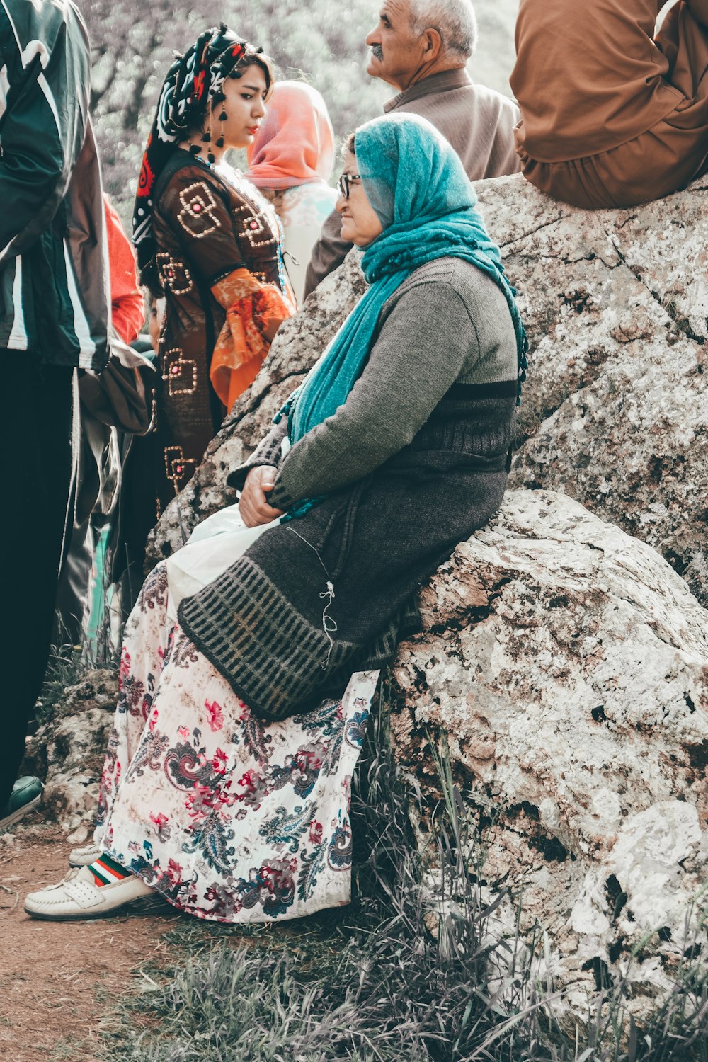 woman in grey long-sleeved shirt and teal scarf sitting on rock during daytime