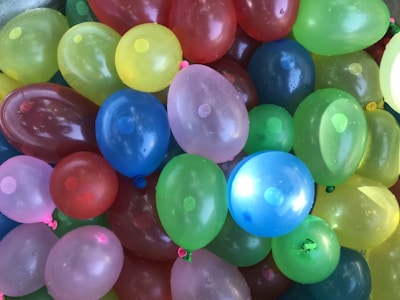 A colorful assortment of water balloons is tightly packed together. They come in a variety of colors, including red, blue, green, yellow, and pink. The balloons are slightly wet, indicating they may have been recently filled with water.