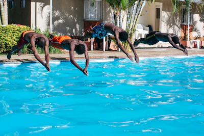 Children diving into a crystal-clear swimming pool with colorful floaties nearby.