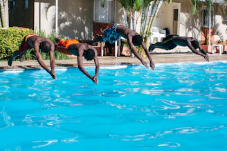 Children diving into a crystal-clear swimming pool with colorful floaties nearby.