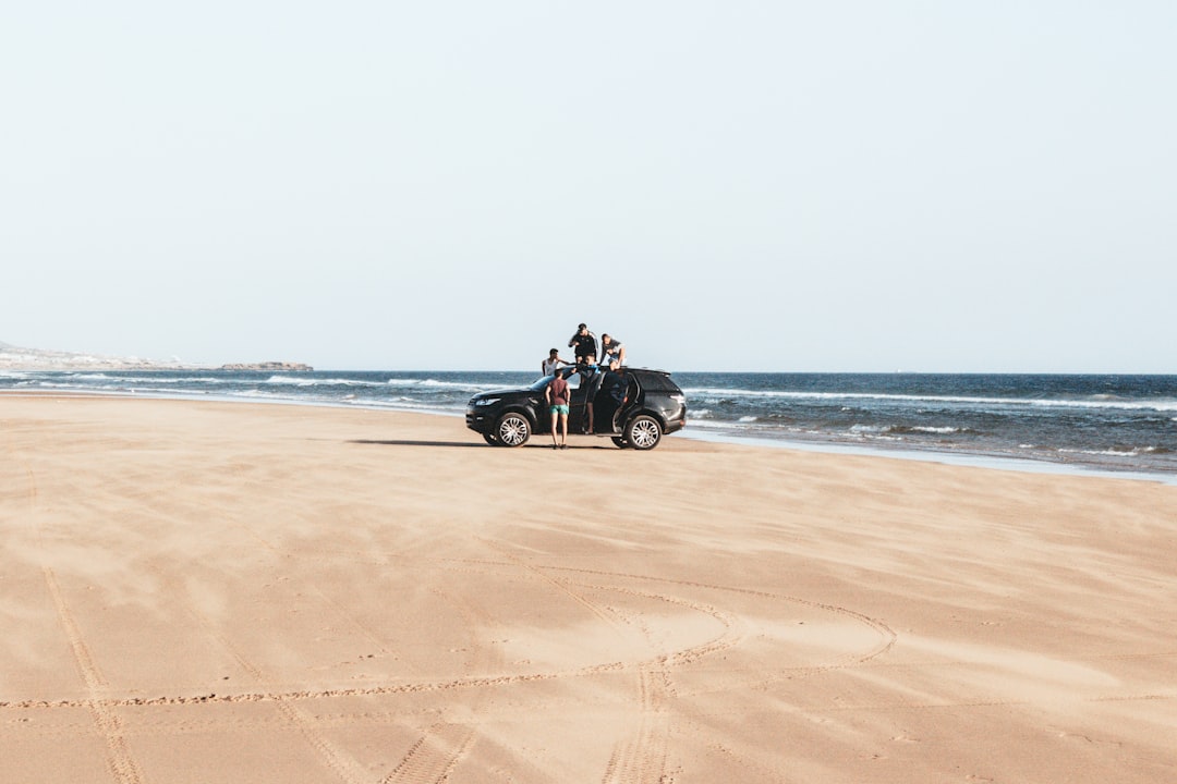 black vehicle parked on shore with four men during daytime