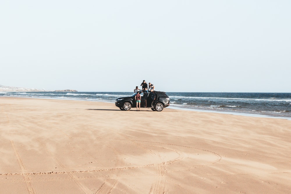 black vehicle parked on shore with four men during daytime