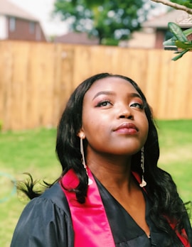 woman wearing black academic coat near tree in front of fence