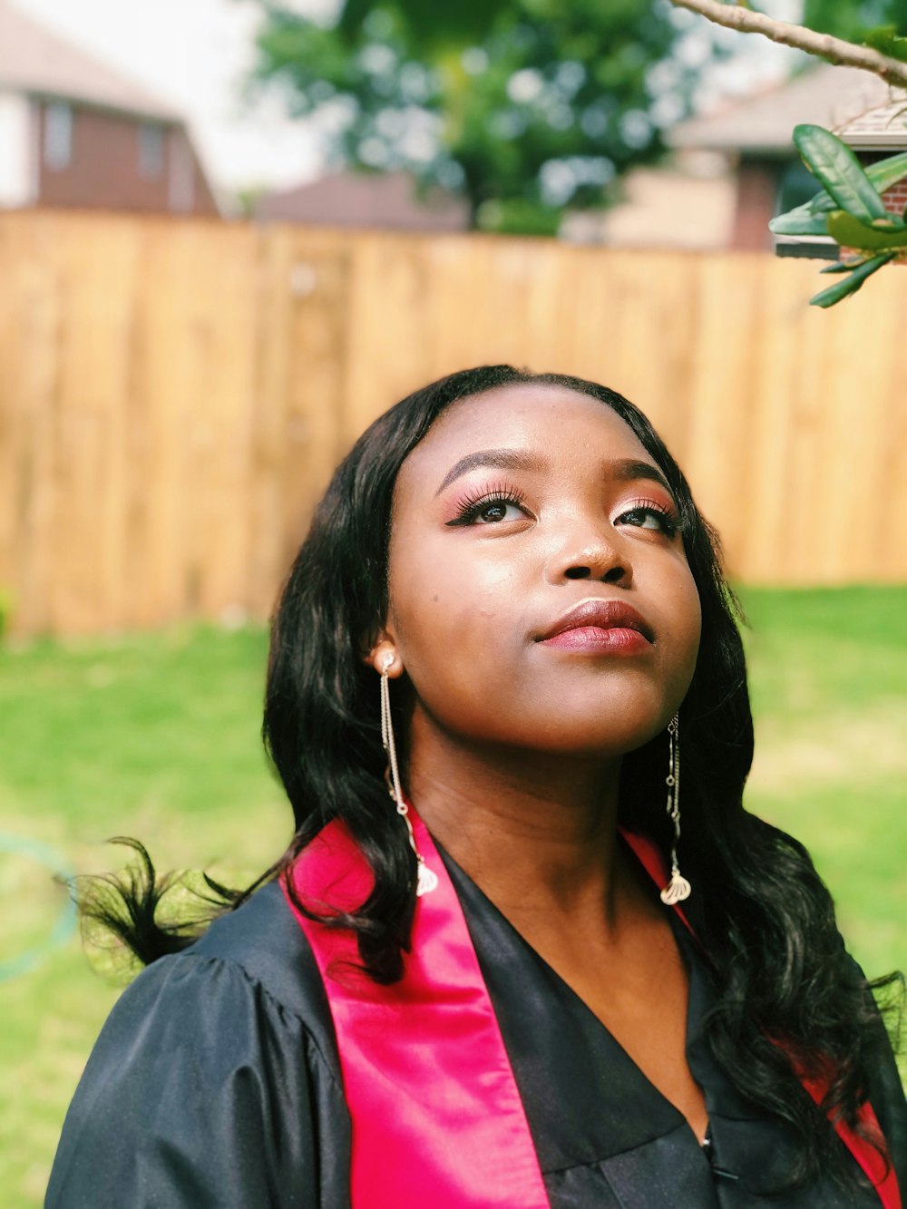 woman wearing black academic coat near tree in front of fence