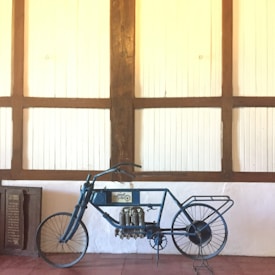 A vintage motorcycle with a unique and exposed mechanical design, showcasing intricate components and metal framework. Positioned against a wooden paneled wall, the scene evokes a sense of history and craftsmanship.