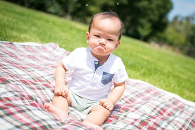 selective focus photography of grumpy face toddler sitting on plaid pad taken during daytime silly zoom background