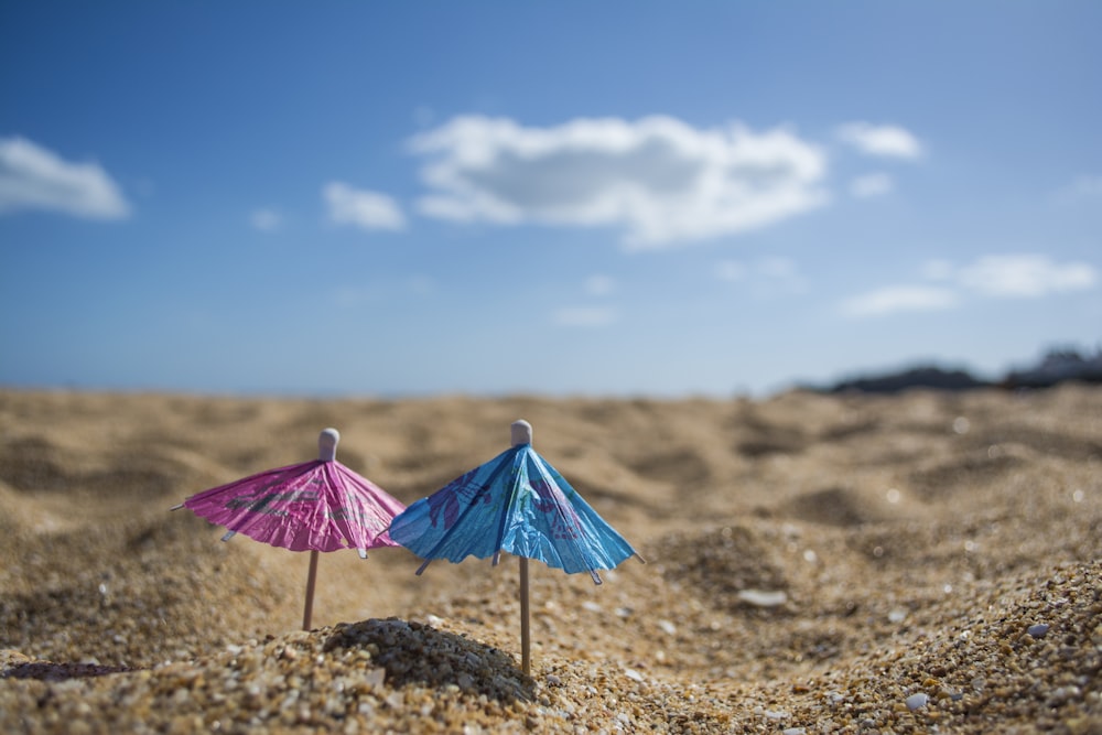 shallow focus photography of cocktail umbrellas pin down in sand