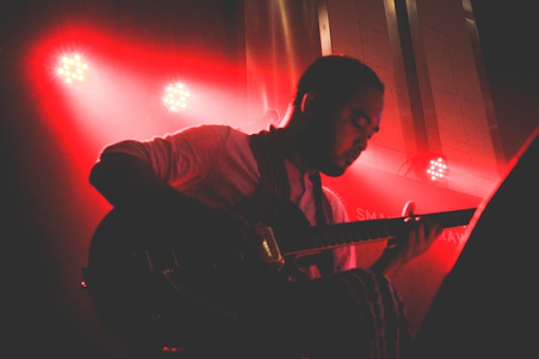 Close-up of a musician passionately playing guitar on stage with dramatic black and red lighting.