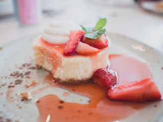A creamy cheesecake topped with a vibrant strawberry glaze and mint leaves.