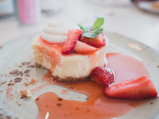 A creamy cheesecake topped with a vibrant strawberry glaze and mint leaves.