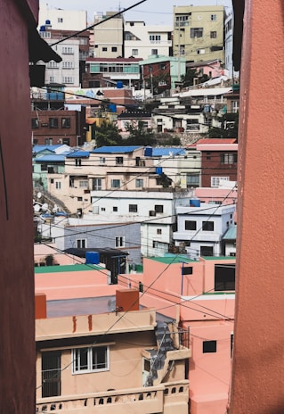 Colorful, densely packed houses line a hilly urban neighborhood, with buildings in various pastel shades of pink, green, and blue. The structures appear closely spaced, and the scene is intersected by numerous power lines crisscrossing the view.