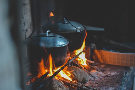 two dutch ovens cooking in fireplace