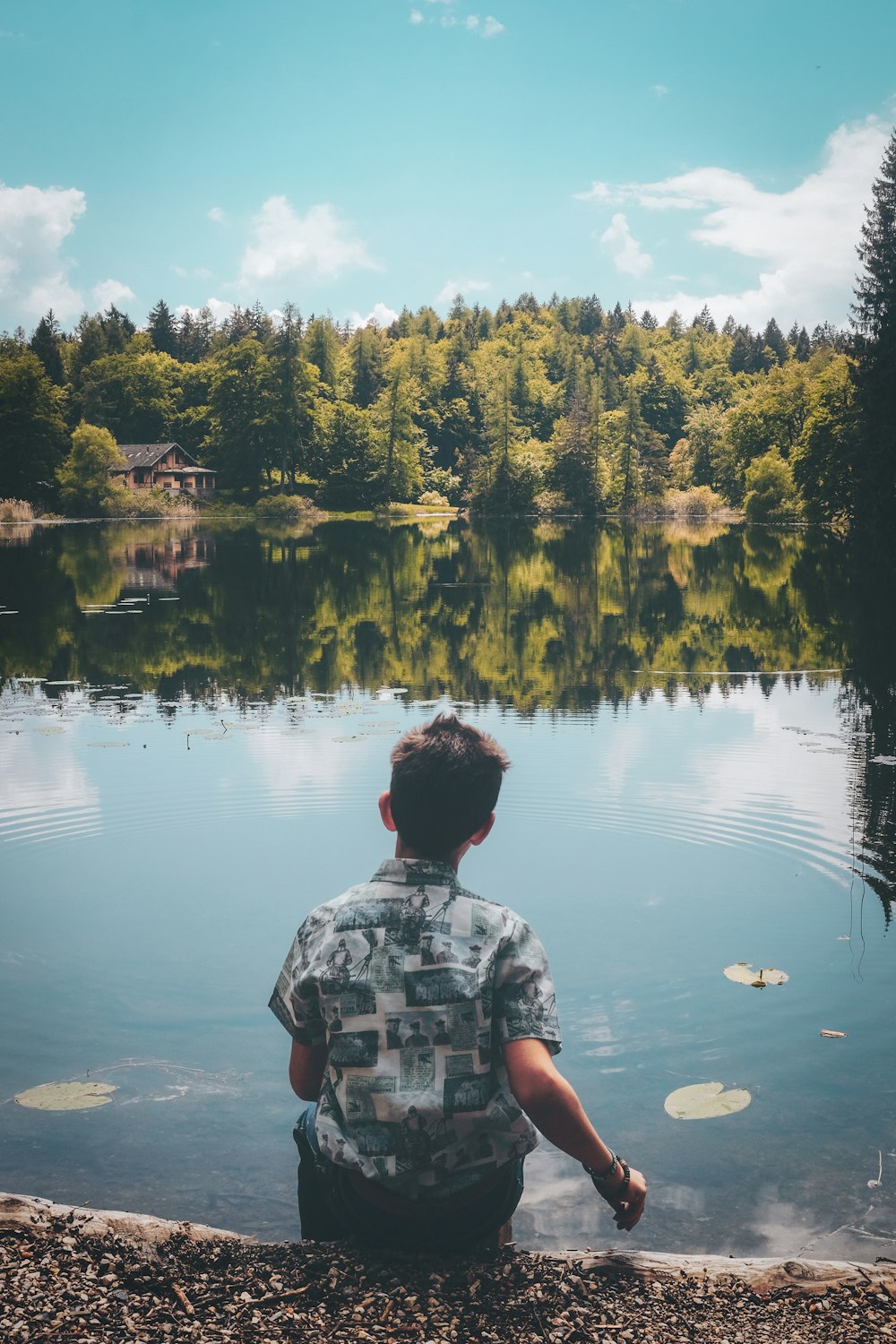 man sitting in front of pond under blue sky