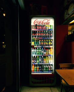Smart cooler with glass door displaying fresh beverages, glowing softly in a modern office corner.
