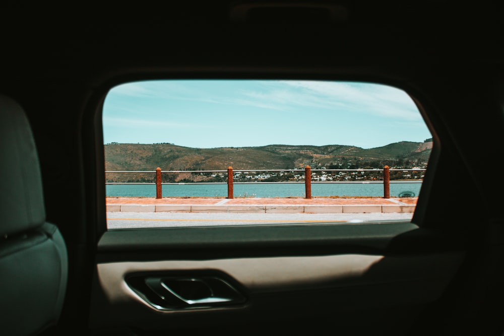 inside vehicle backseat window view of rail near body of water in distant of mountain