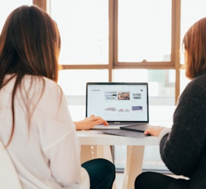 two women talking while looking at laptop computer