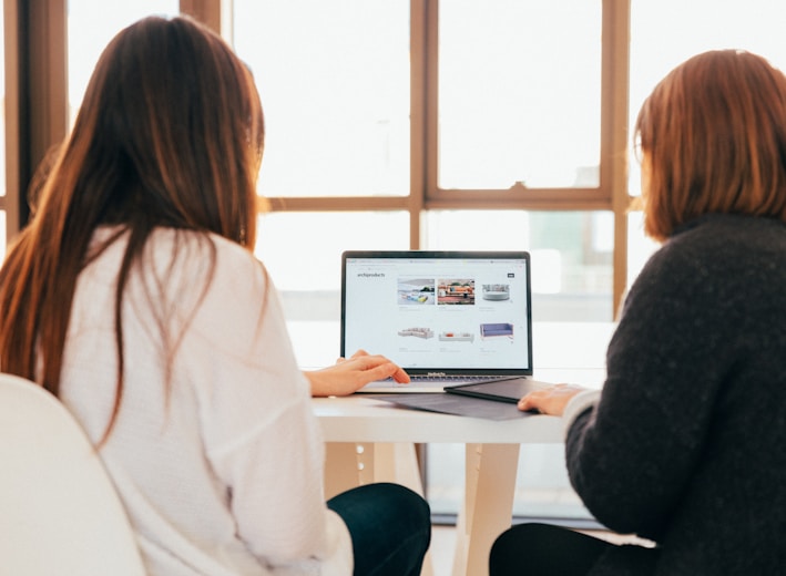 two women talking while looking at laptop computer