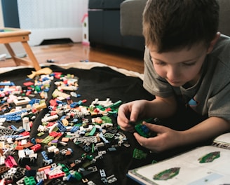 boy in grey crew-neck t-shirt plays LEGO bricks with white manual book