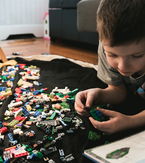 boy in grey crew-neck t-shirt plays LEGO bricks with white manual book