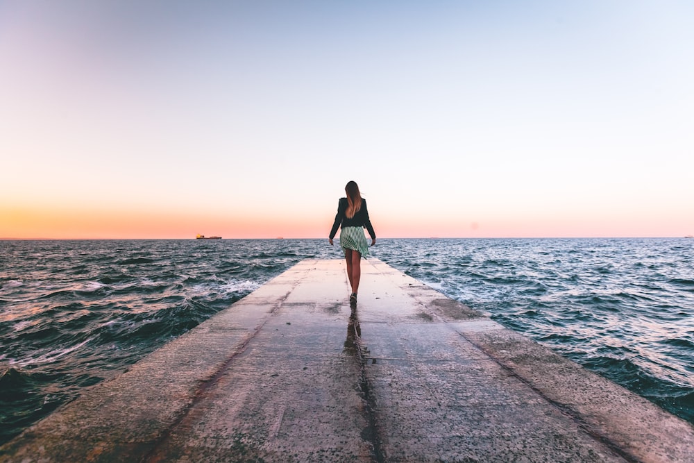 woman walking near dock wooder during daytime