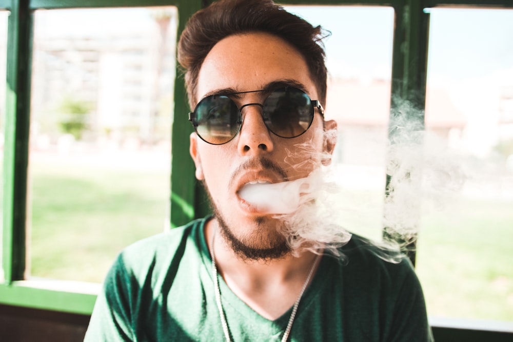 Homem vaping em pé perto da grade verde