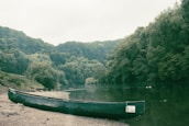 A peaceful riverside scene with lush greenery and a canoe resting on the shore.