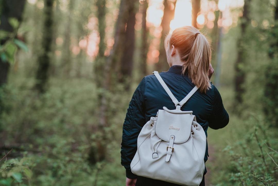 woman carrying white bucket back walking on forest surrounded by trees at daytime