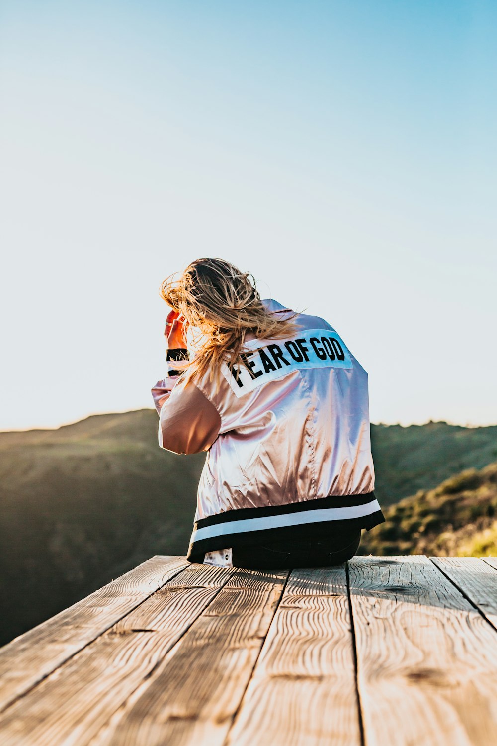 femme portant une veste de couleur argentée assise sur un quai en bois brun pendant la journée