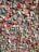 An intricate wall filled with thousands of pieces of colorful chewing gum arranged closely together, creating a textured and vibrant mosaic. Strings of gum add a dynamic, chaotic element to the surface.