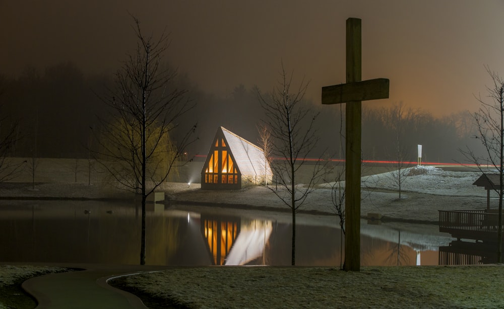 Braunes Holzhaus in der Nähe des Sees und braunes Holzkreuz unter dunklem Himmel