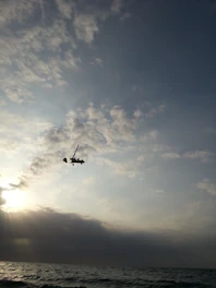 An open cockpit view of a small aircraft soaring above clouds at sunrise.