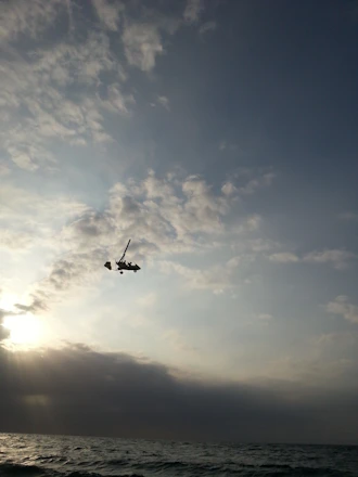 An open cockpit view of a small aircraft soaring above clouds at sunrise.