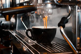Close-up of a barista pouring espresso into a ceramic cup with steam rising.