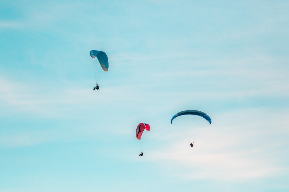 três pessoas no ar com paraquedas
