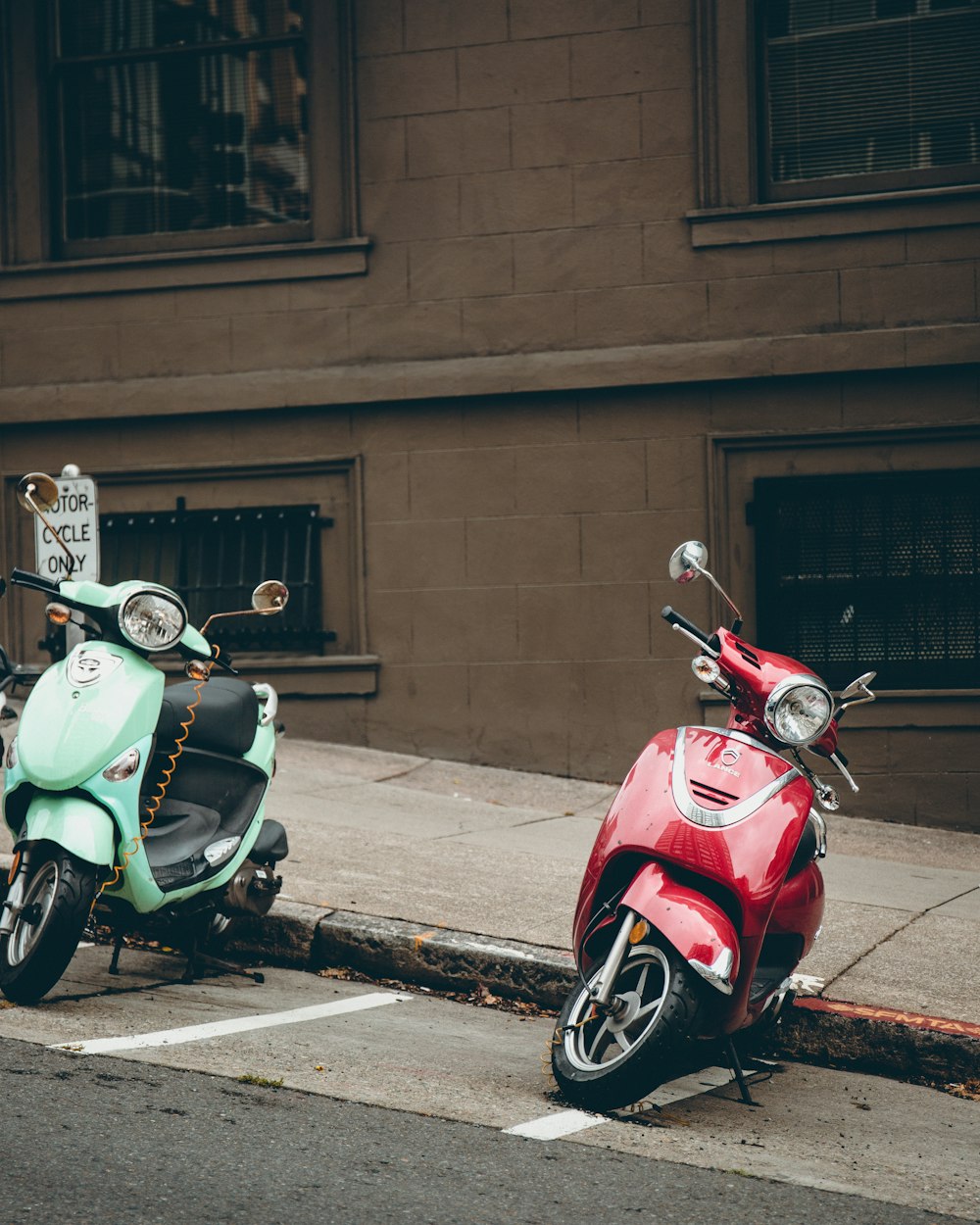Duas motonetas verdes e vermelhas estacionadas na estrada ao lado do prédio
