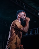 man singing on stage white wearing brown crew-neck shirt