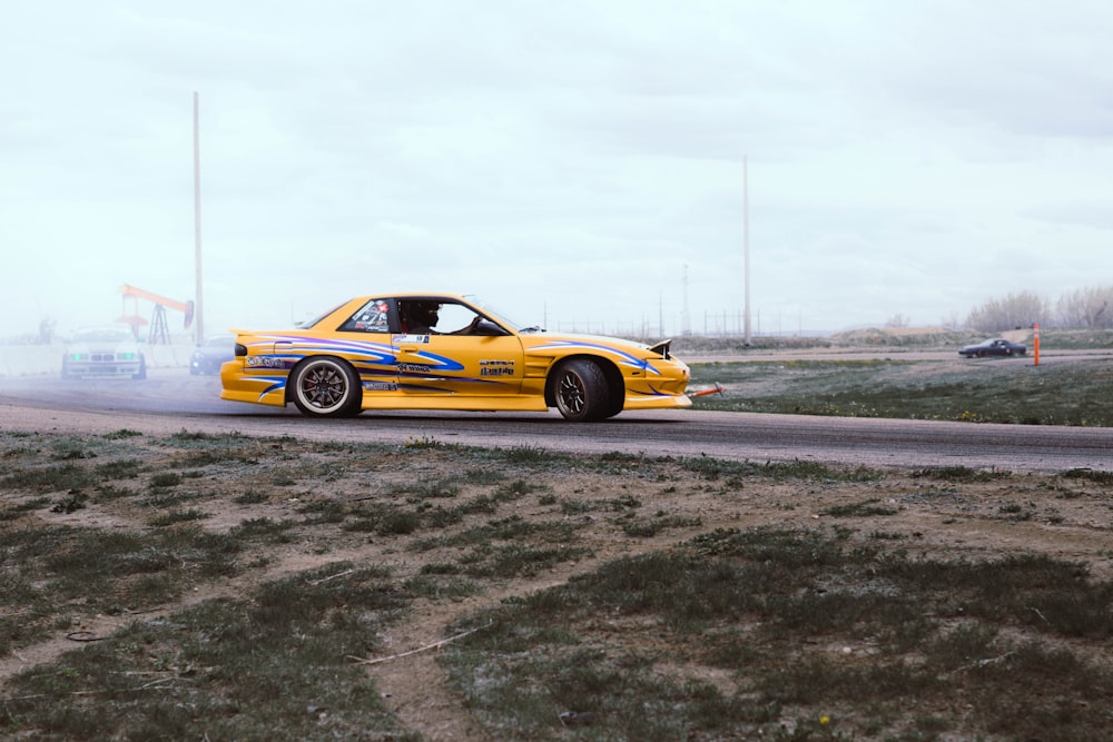 yellow and blue coupe drifts on black asphalt road during daytime