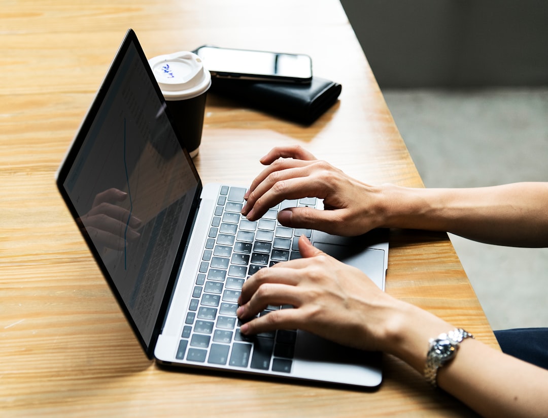 person using gray and black laptop computer on beige desk