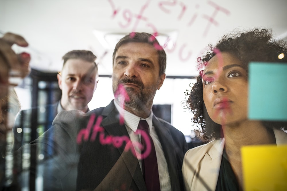 two men and one woman sticking paper on glass board