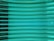 Several horizontal turquoise glass panes are stacked in parallel, creating a layered and reflective surface. The light passing through the glass gives it a luminous and modern appearance.