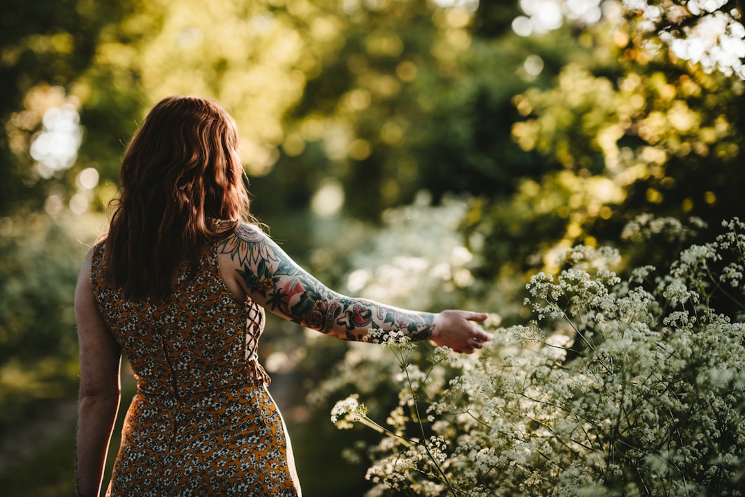 woman standing while holding white petaled flower selective focus photography