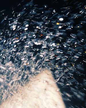A dynamic and abstract display of light reflections and bokeh effects, with sparkling points of light resembling a spray of water or a shower of glitter against a dark background.