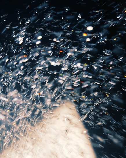 A dynamic and abstract display of light reflections and bokeh effects, with sparkling points of light resembling a spray of water or a shower of glitter against a dark background.